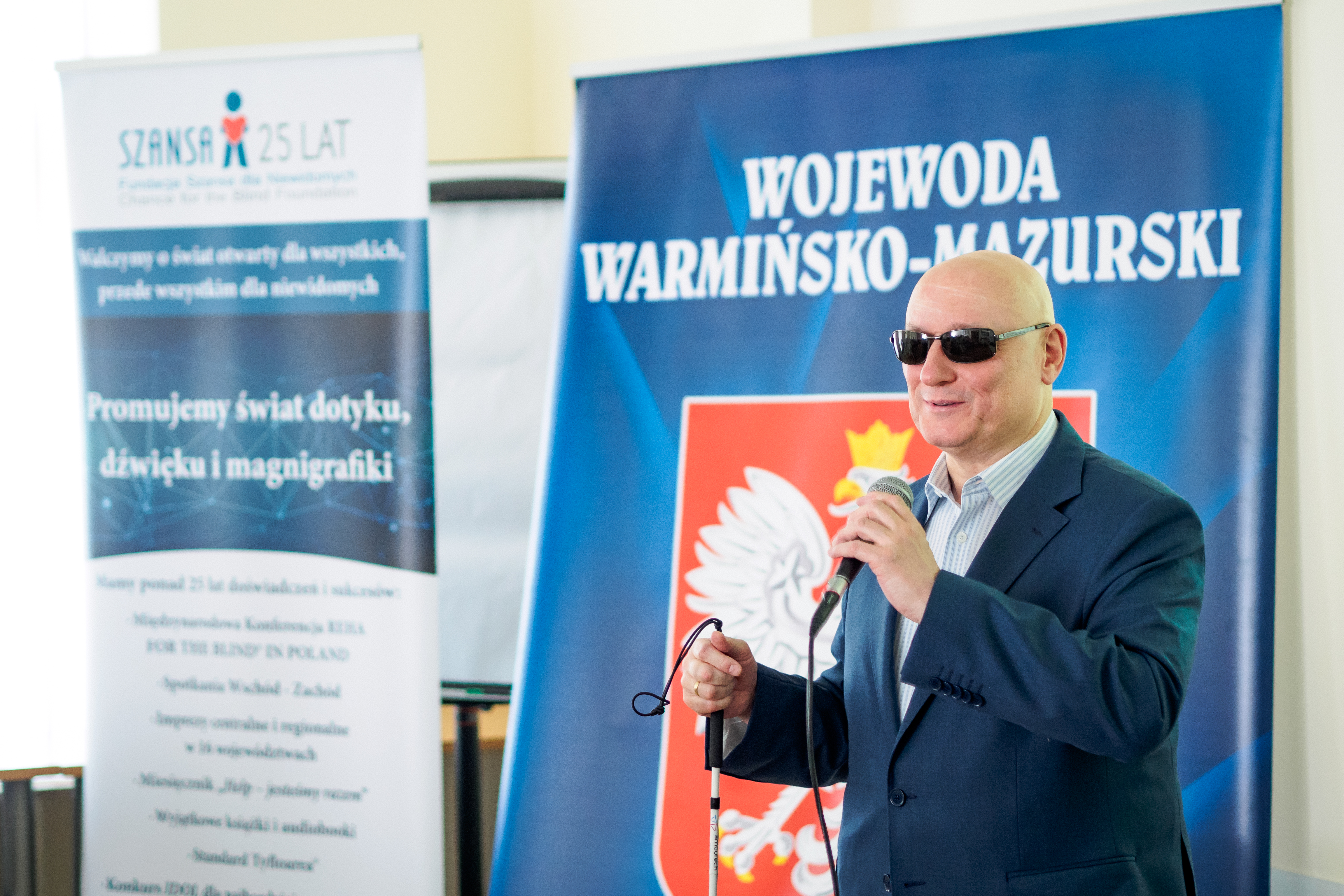 Pan Marek Kalbarczyk. W tle baner Konferencji REHA oraz Wojewody Warmińsko-Mazurskiego.